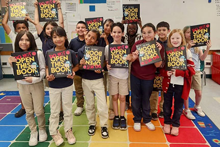 Students hold up their copy of Do Not Open This Book