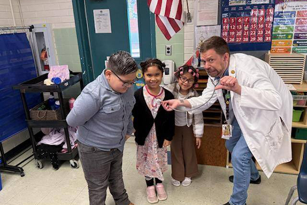 A man dressed as a doctor pretends to liisten to students' hearts