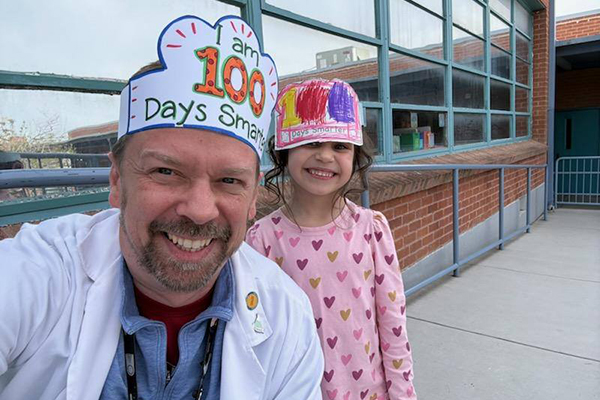 A teacher and one of his students pose in their I am 100 Days Smarter paper crowns