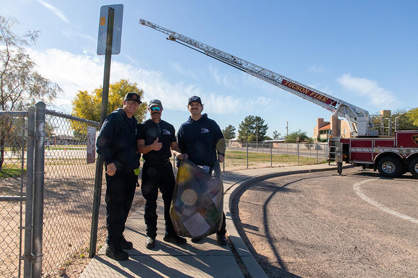 Three firefighters stand under the fire truck ladder, holding a bag of debris from the egg drop