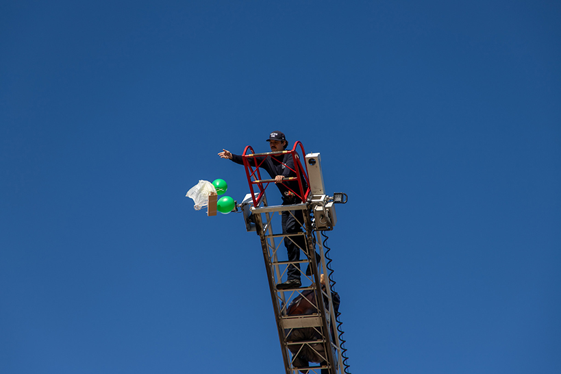 A firefighter stands on the fire truck ladder and drops an egg attached to a balloon