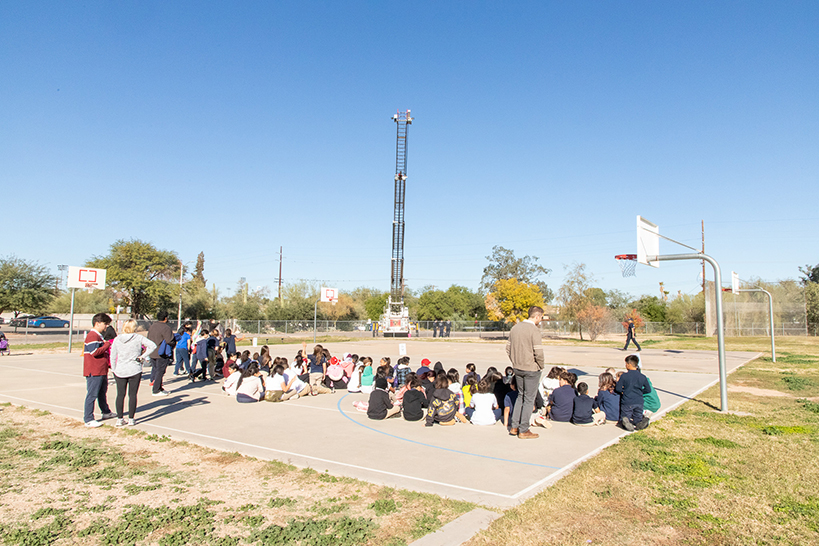 Students sit on the basketball court looking up at the fire truck ladder